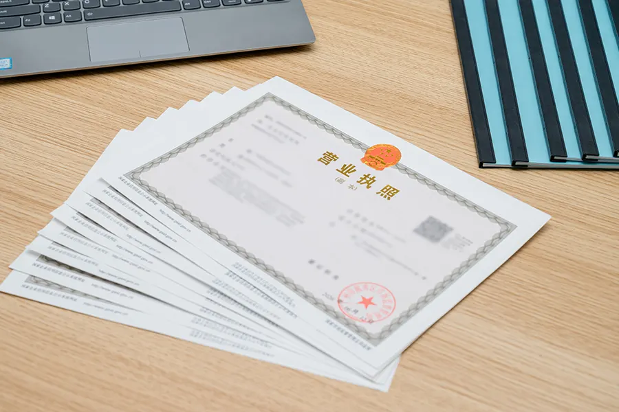 A WFOE business license document placed on a desk with tax filing forms and a computer screen showing compliance software in the background