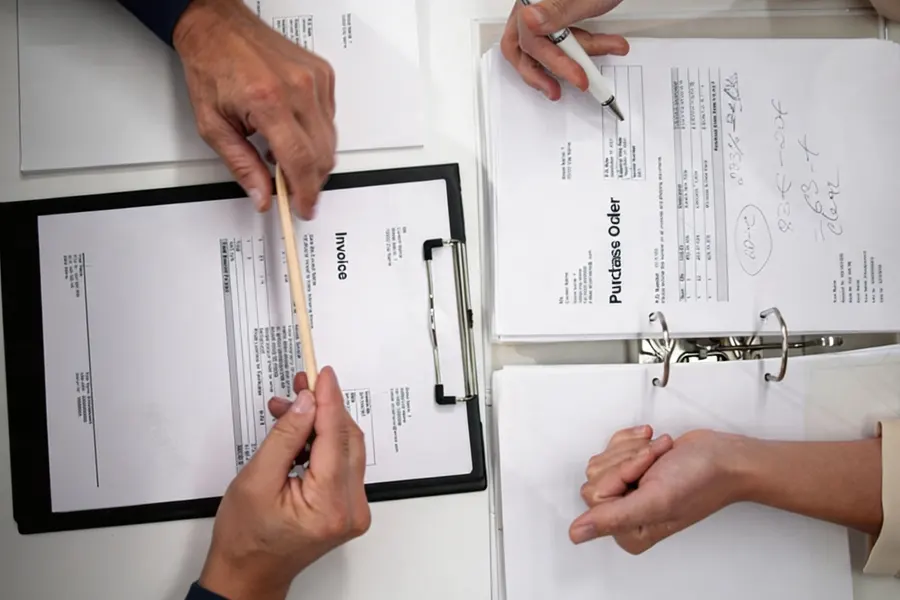 A foreign-owned trading company manager reviewing a stack of invoices and export declarations in a small office with product samples on shelves behind
