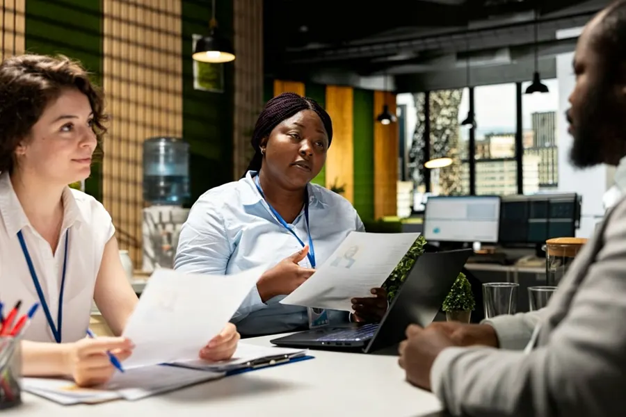 HR manager at a desk reviewing a foreign employee work permit application folder with a hiring timeline printed on the wall